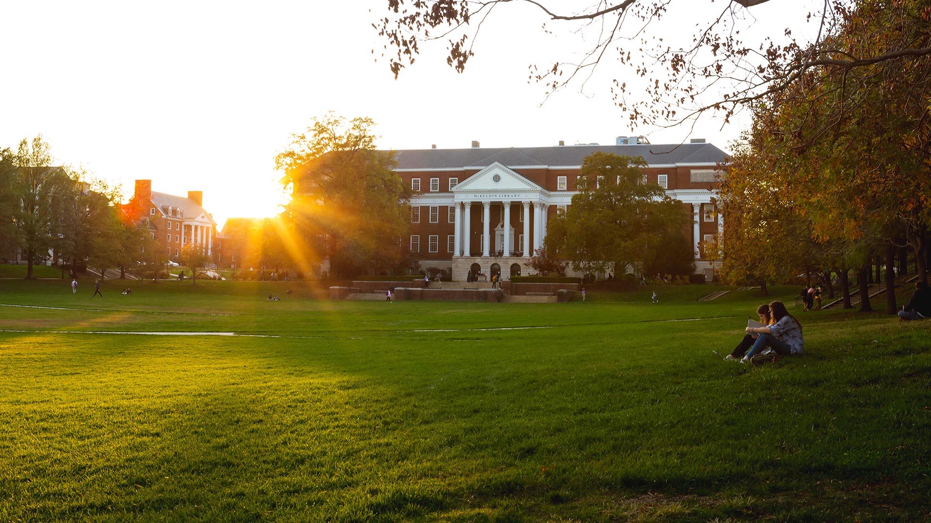Photo of McKeldin Mall at sunset with two students sitting on the side by Stephanie S. Cordle.